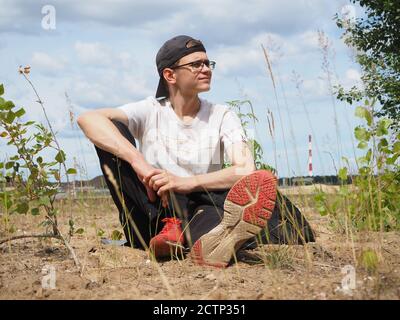 Un jeune homme est assis dans un parc sur le sable. Banque D'Images