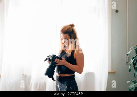 Photo d'une belle fille utilisant un appareil photo - une magnifique jeune femme aux cheveux longs souriant tout en regardant sur l'écran d'un appareil photo Banque D'Images