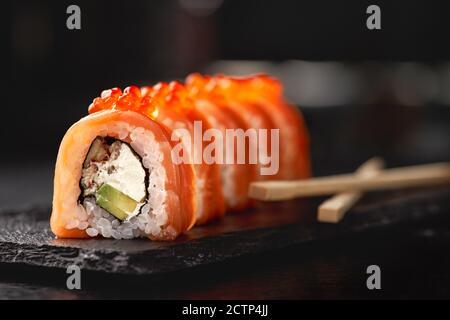 Sushi roll maki futo cuisine japonaise sur une assiette en pierre noire dans les mains d'un serveur. Gros plan Banque D'Images