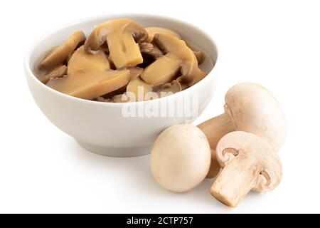 Champignons de Paris tranchés en conserve dans un bol en céramique blanc à côté de champignons de Paris frais isolés sur blanc. Banque D'Images