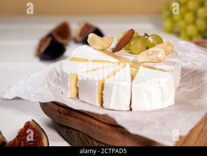 Fromage Camembert sur bois, branche de raisin vert, tranche de figues et noix. Banque D'Images