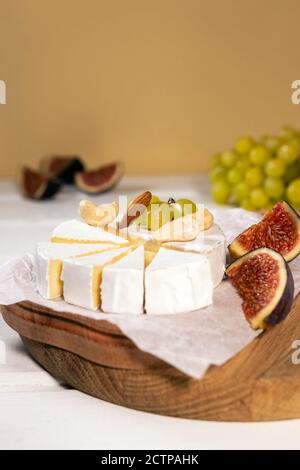 Fromage Camembert sur bois, branche de raisin vert, tranche de figues et noix. Banque D'Images