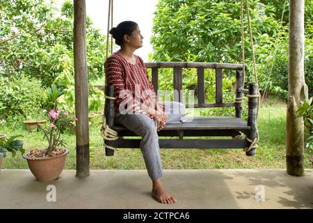 Une jolie femme assise sur une balançoire en bois lisant un réservez dans un environnement magnifique Banque D'Images