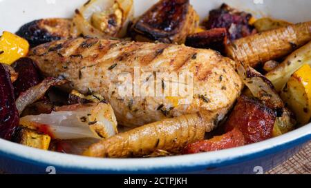 Un poulet grillé est assis dans une assiette en céramique, à côté de divers légumes-racines. Les lignes rouges du motif de la poêle sont clairement visibles. Banque D'Images