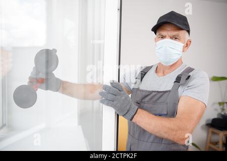 L'homme de travail dans le masque médical installe les fenêtres en plastique upvc et portes blanches avec ventouse de levage Banque D'Images