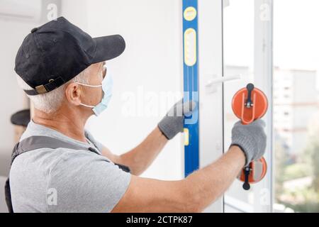 L'homme de travail dans le masque médical installe les fenêtres en plastique upvc et portes blanches avec ventouse de levage Banque D'Images