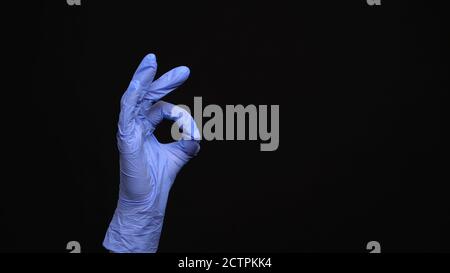 La main femelle dans un gant médical en latex rend un ok geste isolé sur fond noir Banque D'Images