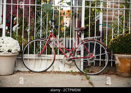 Un vélo rouge vintage attend à l'extérieur contre une clôture entourée de jardinières et de fleurs. Banque D'Images