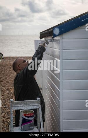 Homme peignant une cabane de plage à Ferring, West Sussex. Banque D'Images