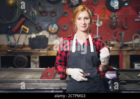 Belle jeune femme artisan ingénieur se tient en tablier sur fond d'outils de fabrication Banque D'Images