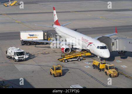 Un avion à réaction de passagers d'Austrian Airlines stationné à l'aéroport de Heathrow avec des véhicules de support adjacents et un pont pneumatique connecté Banque D'Images