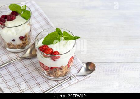 Granola maison avec tranches de fraises dans des verres transparents sur fond clair. Plat végétarien. Petit déjeuner sain. Copier l'espace. Banque D'Images