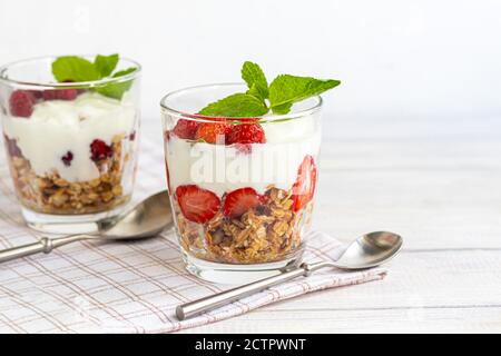 Granola maison avec tranches de fraises dans des verres transparents sur fond clair. Plat végétarien. Petit déjeuner sain. Copier l'espace. Banque D'Images