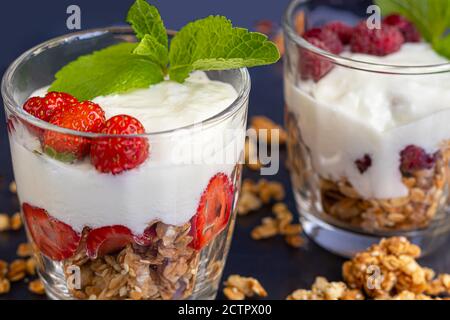 Granola maison avec tranches de fraises dans des verres transparents sur fond sombre. Plat végétarien. Petit déjeuner sain. Copier l'espace. Banque D'Images