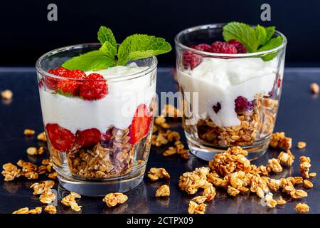 Granola maison avec tranches de fraises dans des verres transparents sur fond sombre. Plat végétarien. Petit déjeuner sain. Copier l'espace. Banque D'Images