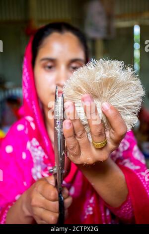 Une femme qui fait de l'artisanat lisse les fibres d'un bananière avec des ciseaux à Madhupur, Tangail, Bangladesh. Banque D'Images