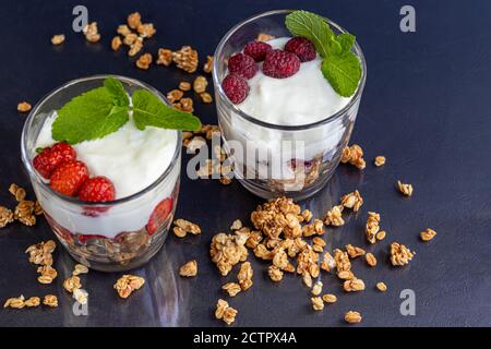 Granola maison avec tranches de fraises dans des verres transparents sur fond sombre. Plat végétarien. Petit déjeuner sain. Copier l'espace. Banque D'Images