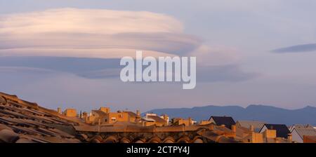 Grands nuages lenticulaires sur les toits des maisons résidentielles dans un logement au coucher du soleil Banque D'Images