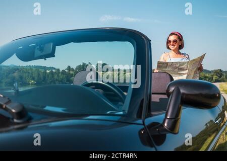 Femme à la recherche d'une route droite dans la feuille de route pendant son voyage automatique dans la voiture cabriolet convertable. Image du concept de déplacement et de navigation. Banque D'Images