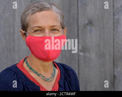 Une femme caucasienne d'âge moyen aux cheveux courts porte un masque rouge non médical fabriqué à domicile pendant la pandémie de 2019/20 du virus corona. Banque D'Images