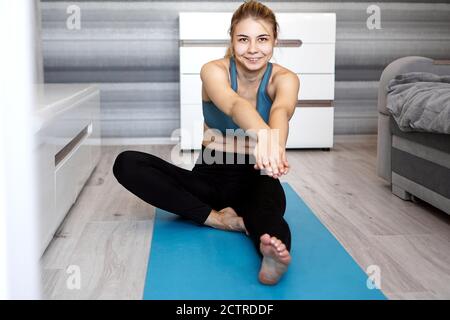 Sport, entraînement et style de vie concept - femme étirant la jambe sur le tapis de yoga bleu à la maison dans le salon Banque D'Images