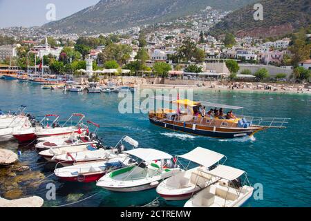 Un bateau charter passe devant de petits bateaux à moteur, au premier plan, car il quitte le port de Kalkan en Turquie. Kalkan est une destination de vacances populaire an Banque D'Images