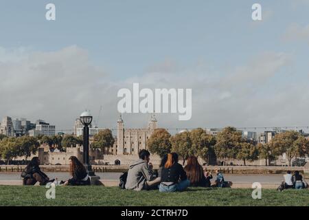 Londres, Royaume-Uni - 25 août 2020 : personnes assises socialement à distance sur la rive de la Tamise, la Tour de Londres, un château historique et le Palais Royal Banque D'Images