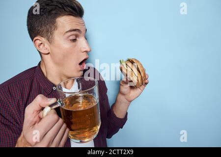 homme gai ivre avec une tasse de bière et un hamburger à la main régime alimentaire style de vie fond bleu Banque D'Images