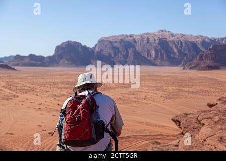 Un touriste d'âge moyen occidental portant un sac à dos rouge et chapeau solaire est debout sur le bord d'un grès falaise donnant sur les vastes terres désertiques Banque D'Images