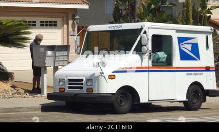 Un employé du service postal des États-Unis apporte le courrier à une boîte aux lettres dans un quartier de banlieue. Il porte un masque en raison de la réglementation Covid-19. Banque D'Images