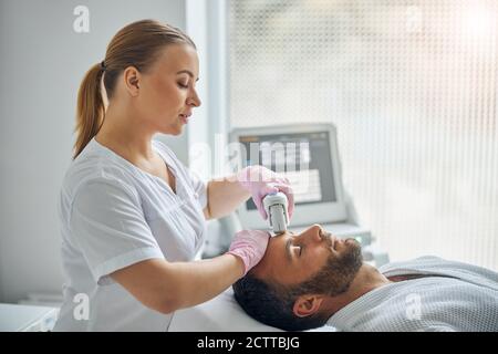 Charmante femme cosmetologiste traitant la peau masculine avec un appareil laser Banque D'Images