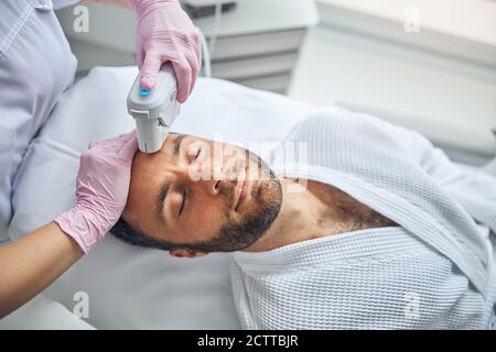 Esthéticienne féminine traitant la peau masculine à l'aide d'un dispositif laser Banque D'Images