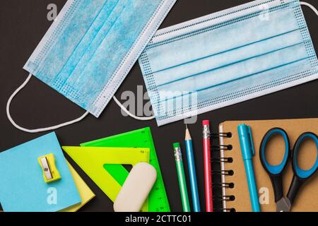 Fournitures scolaires et masques médicaux sur un tableau noir, vue du dessus. Concept sur le thème du port de masques dans les établissements d'enseignement pendant le quaran Banque D'Images