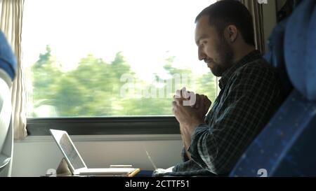 Homme excité vérifiant le travail sur une tablette dans le train étant satisfait du résultat. Banque D'Images