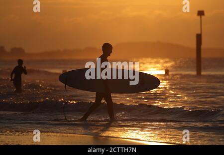 Un surfeur se promène dans la mer tandis que le soleil se lève sur la plage de Boscombe à Dorset. Banque D'Images