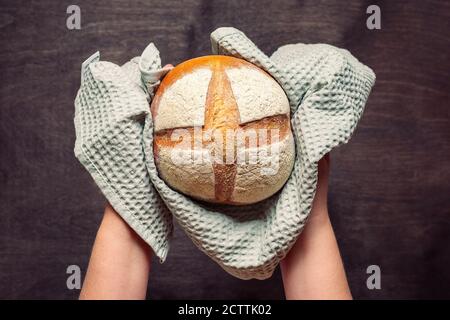 les mains des femmes contiennent le pain de levain fraîchement cuit dans la serviette de Four sur table en bois bleu vue sur le dessus Flat Lay fait maison pâtisserie Banque D'Images