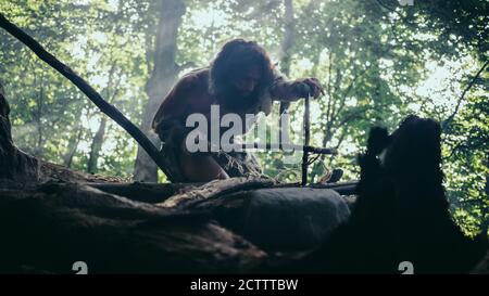 Silhouette de Caveman primitif portant une peau d'animal essayant de faire un feu avec la méthode de forage de noeud. Neanderthal Kindle Premier feu fait par l'homme chez l'homme Banque D'Images