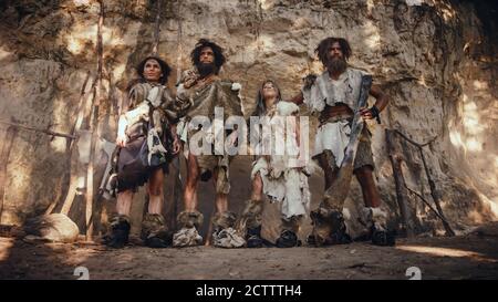 Tribu de quatre chasseurs-cueilleurs portant la peau d'animal tenant des outils de pierre à ébréché, posent à l'entrée de leur grotte. Portrait de deux hommes et deux Banque D'Images