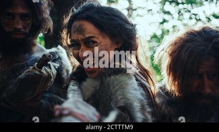 Le leader féminin et deux guerriers de Cavemen préhistoriques menacent l'ennemi avec la lance à pierre, Scream, défendant leur grotte et leur territoire dans le préhistorique Banque D'Images