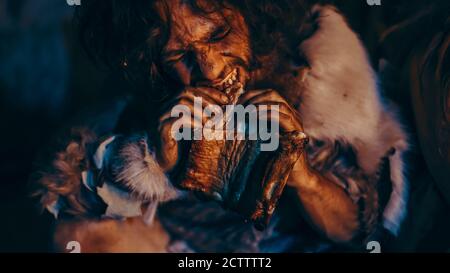 Gros plan Portrait de Tribe leader portant une peau animale manger dans une grotte sombre effrayante la nuit. Neanderthal ou Homo Sapiens cuisine familiale viande animale Banque D'Images