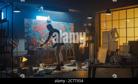 Talentueux artiste masculin énergique et violent utilisant la brosse de peinture il crée le chef-d'œuvre moderne de la peinture à l'huile. Studio créatif sombre et désordonné Banque D'Images