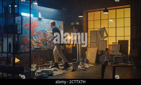 Talentueux artiste masculin énergique en utilisant le pinceau il crée le chef-d'œuvre moderne de la peinture à l'huile. Studio créatif sombre et désordonné avec grand Banque D'Images