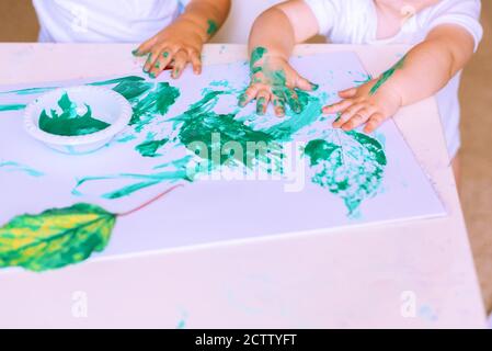 Gros plan de la main petit enfant dessin avec de la peinture verte sur les feuilles d'automne. Joli adorable bébé enfant peinture à la table avec aquarelles. Banque D'Images