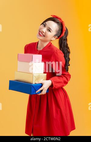 Portrait d'une jeune fille mignonne en tenue rouge pile de boîtes présentes isolée sur fond orange Banque D'Images