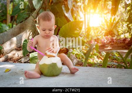 Bébé pésif et passionné lors de vacances tropicales. Mange et boit de la noix de coco verte jeune avec une cuillère Banque D'Images