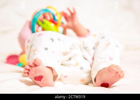 Bébé repose avec les coeurs sur leurs pieds. Un nouveau-né est allongé sur le lit et joue des jouets Banque D'Images