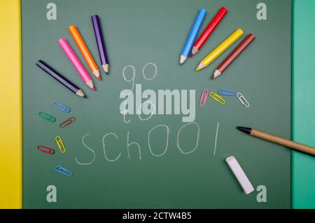 Sur un tableau vert aller à shool dit des crayons, des trombones de couleur, et un stylo. Concept scolaire, année scolaire. Un cadre magnifique et amusant pour l'école. Banque D'Images