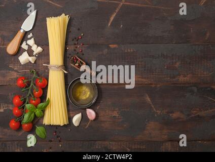 Spaghetti crus aux tomates cerises et au basilic, ail et huile au parmesan et sel et poivre sur fond de bois. Espace pour le texte Banque D'Images