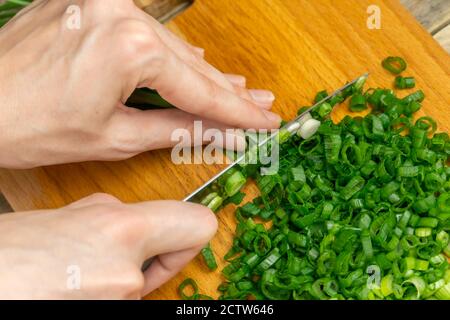 Les mains des femmes coupent des oignons verts avec un couteau sur un Panneau en bois gros plan Banque D'Images