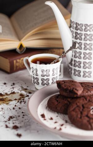 Café renversé sur la table. Composition de cookies au chocolat sur l'assiette, la tasse de café, la cafetière et les livres. Photographie alimentaire. Petit-déjeuner Banque D'Images